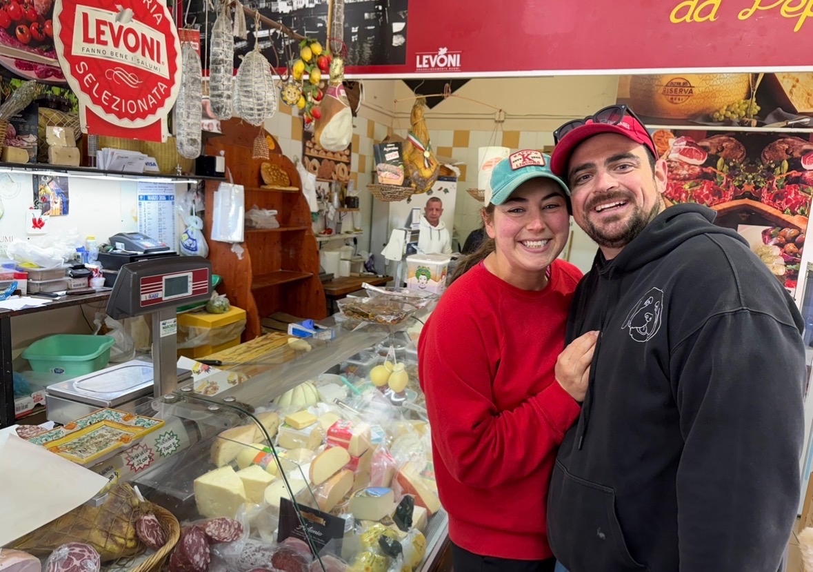 Molly and a companion visiting a cheese and salumi shop in Sicily